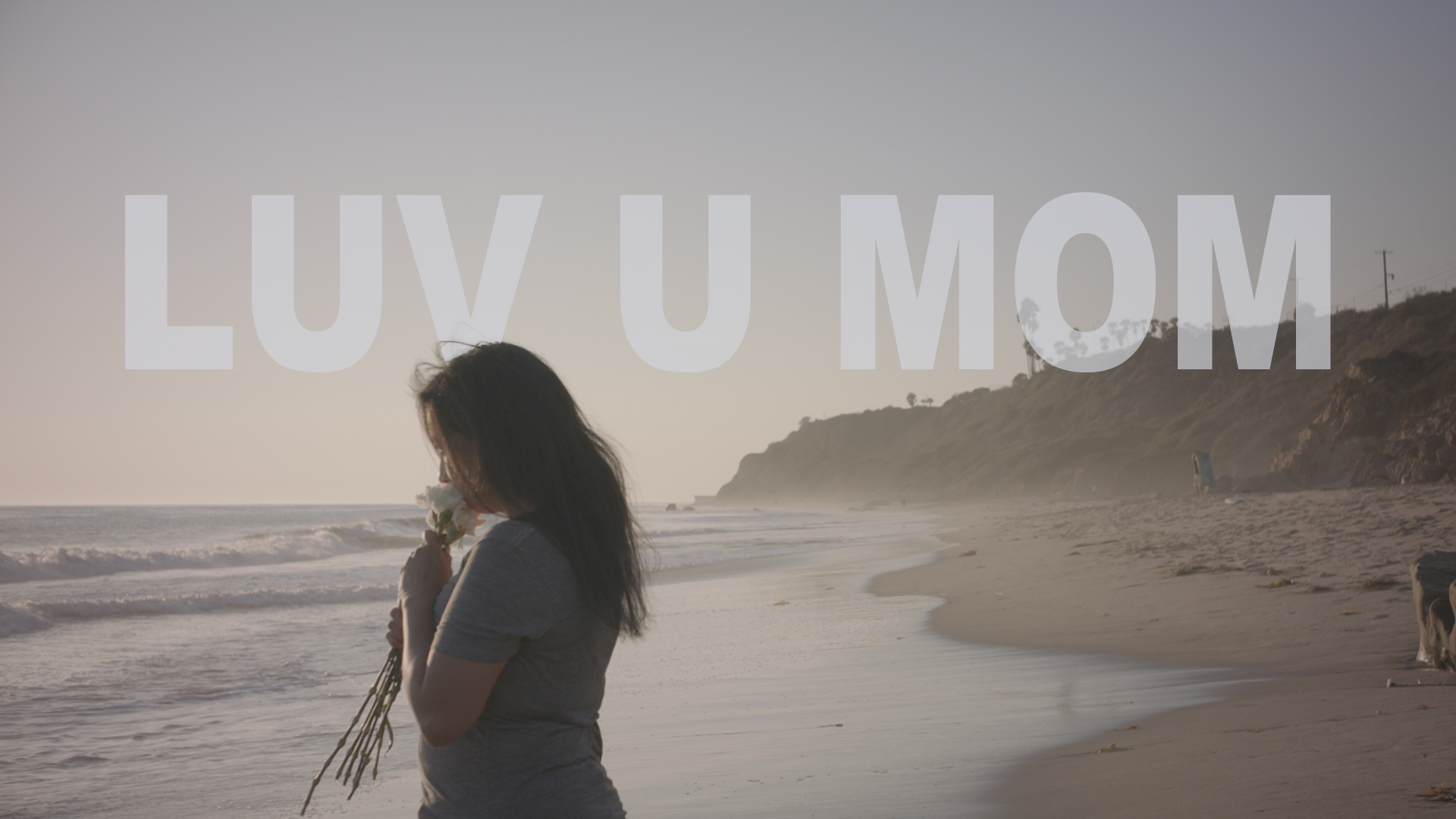 Luv U Mom Logo Image of a woman in silhouette standing on the shore